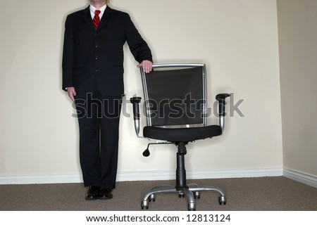 Businessman in full suit and tie stands next to empty office chair