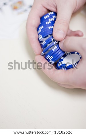 man is holding a set of blue gambling chips in his hands waiting to make his bet with cards blurred in the background