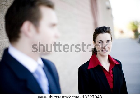 attractive businesswoman and businessman standing looking at each other wearing formal business wear