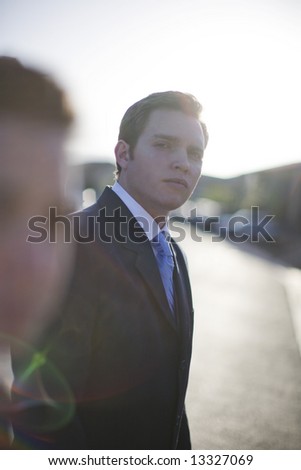businessman standing wearing suit with sun behind him and woman in front
