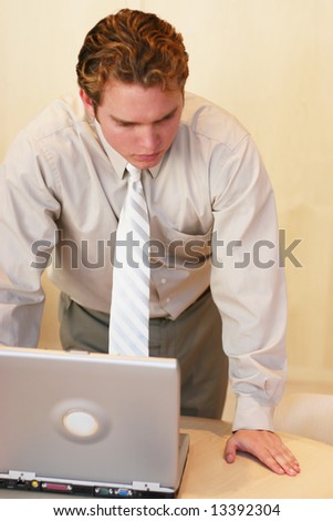 front view of businessman in tan shirt standing over open laptop computer