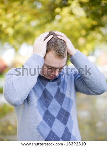 young student stressed out places hand on top of head with trees in background