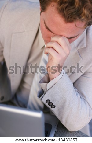 businessman in tan suit leaning over laptop with hand on forehead