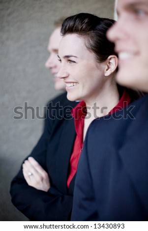profile view of three businesspeople standing in line wearing formal clothing smiling