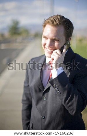 businessman standing outside talking on his cell phone and smiling about the conversation while wearing a dark suit