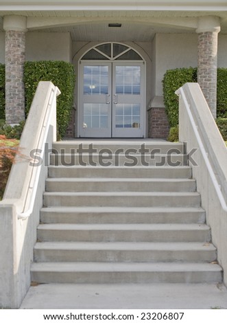 many stairs lead up to a glass door on a building outside with bricks on the building and a landscaped bushes on the sides of the door
