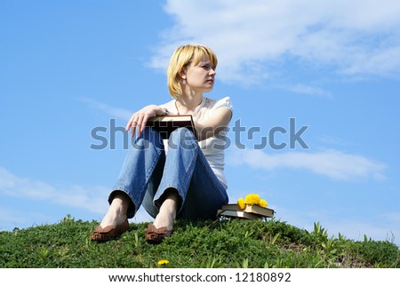 female student outdoor on green grass with books and blue sky on background