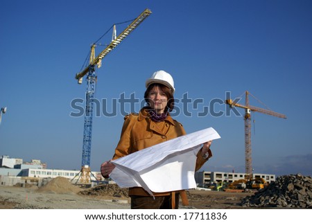 Pretty woman architect holding blueprints and standing in the building site