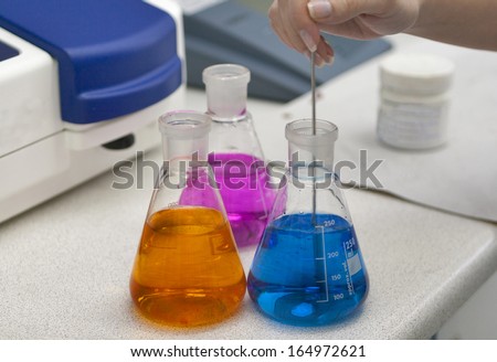 Flasks with colored chemicals and human hand.