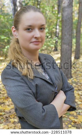 pretty young woman in a gray business dress standing in the autumn forest half-turned with arms crossed