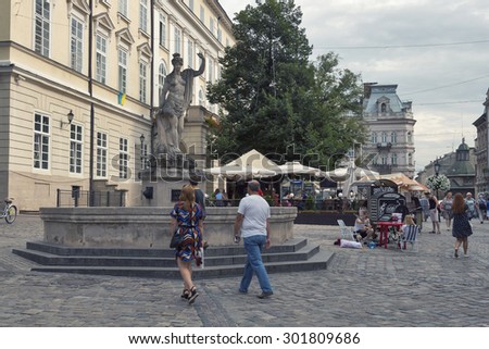 LVIV, UKRAINE - JULY 29, 2014: Pedestrians walk in front of ancient statue of Amphitrite on Market (Rynok) Square, the central square and most popular touristic place in historical part of old town.