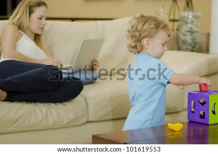 Cute blond boy playing with a puzzle while mom works