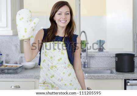 Pretty housewife waving with oven gloves on