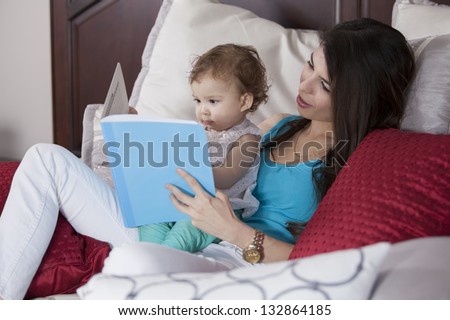 Young latin mother reading a story to her baby girl before going to bed