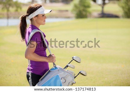 Beautiful female golfer carrying a golf bag and looking towards copy space