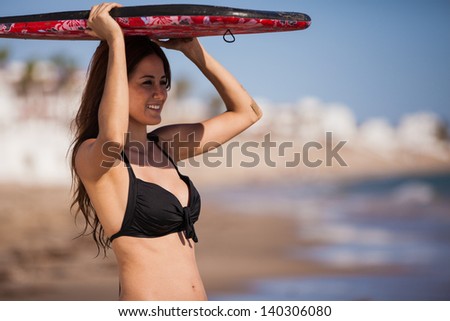 Beautiful young woman holding a body board on top of her head to cover from the sun and smiling