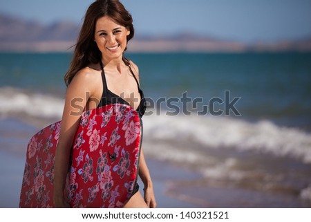 Cute young woman holding a body board and smiling at the beach