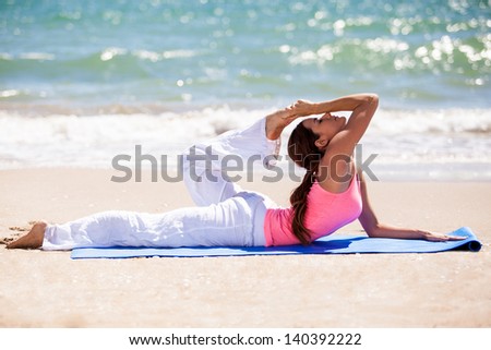Cute flexible Latin woman stretching with a yoga pose at the beach