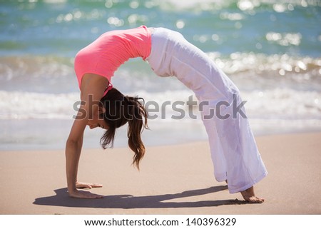 Beautiful young woman arching her back and standing backwards on hands and feet while doing yoga at the beach
