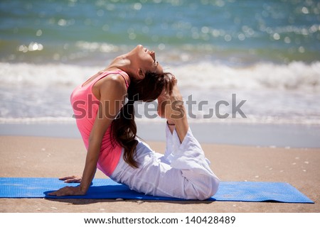 Young woman arching her back and touching her head with her feet for a yoga pose at the beach