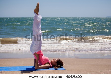 Pretty young woman doing some yoga at the beach and standing on her back and head