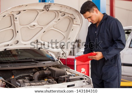 Handsome mechanic using a tablet computer for work in an auto shop