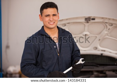 Portrait of a young Hispanic mechanic holding a wrench at an auto shop