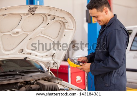 Young Latin mechanic using a multimeter to check a battery at an auto shop