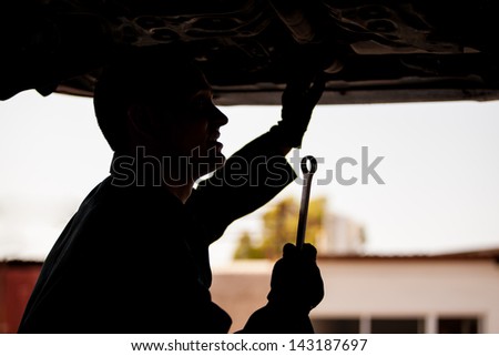 Silhouette of a young mechanic holding a wrench under a suspended car at an auto shop