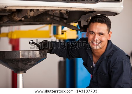 Happy young mechanic draining engine oil at an auto shop for an oil change