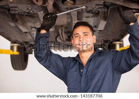 Portrait of a handsome young mechanic working on a suspended car at an auto shop and smiling