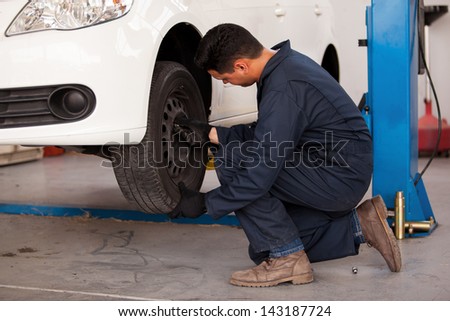 Young mechanic rotating tires of a suspended car at an auto shop