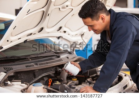 Young Hispanic mechanic changing the oil filter of a car at an auto shop