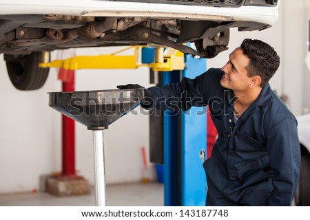 Happy young mechanic changing the oil of a car at an auto shop