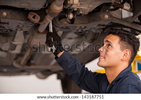 Young mechanic using a wrench and fixing a suspended car at an auto shop
