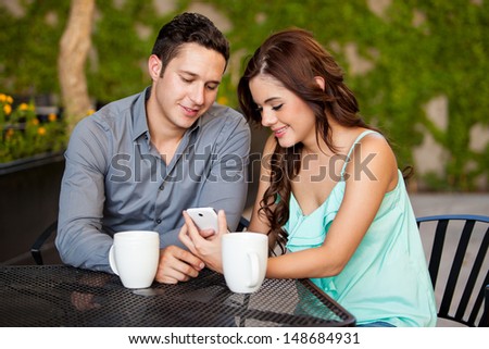 Cute Hispanic couple looking at a cell phone together on a date at a terrace