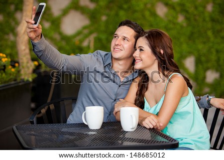 Young attractive couple taking a photo with a cell phone during their first date at a cafe