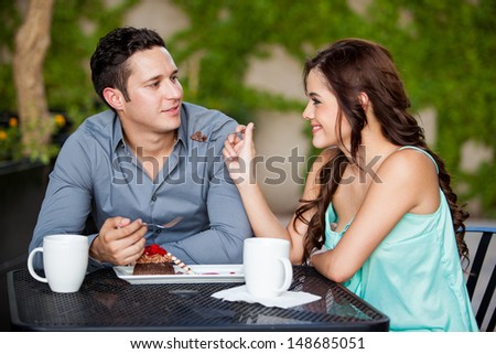Beautiful young brunette sharing cake with her date at a coffee shop outdoors
