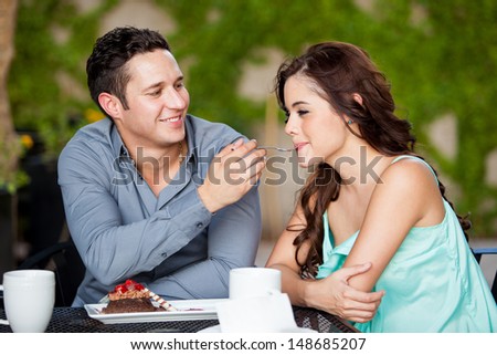 Happy Hispanic couple sharing cake on a date at a cafe outdoors
