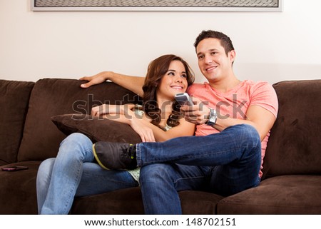 Cute brunette and her boyfriend relaxing on the couch and watching some TV