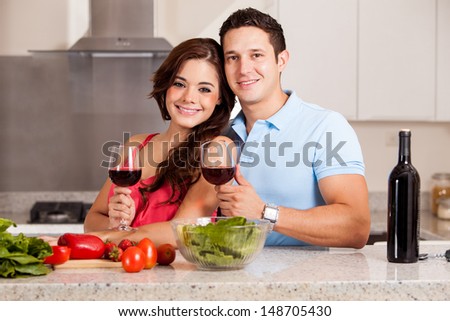 Cute Hispanic couple cooking dinner together and drinking a glass of wine