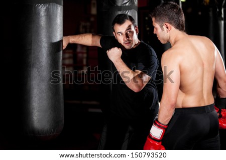 Latin Boxer And His Coach Practicing Some Moves On A Punching Bag At A Gym