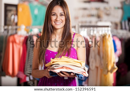 Happy Latin woman holding a pile of new clothes that she wants to try on in a clothing store
