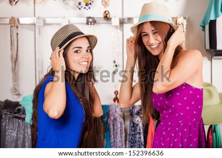 Pretty Latin female friends trying some hats on for fun in a clothing store