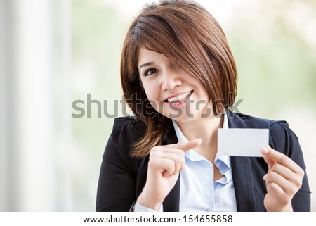 Happy young businesswoman holding a business card in one hand and pointing at it with the other