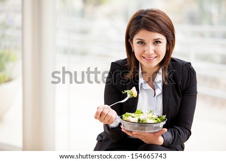 Happy young business woman enjoying a healthy salad at work