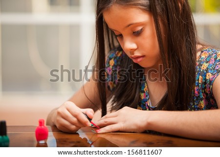 Closeup of a little Hispanic girl borrowing her mom\'s nail polish to paint her nails
