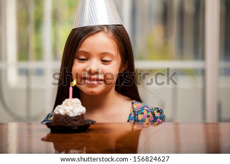 Beautiful little girl on a party hat making a birthday wish on her birthday