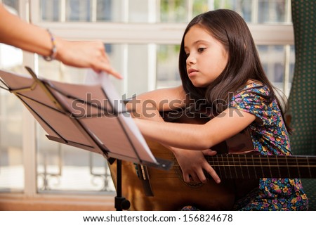Cute Little Girl Playing The Guitar During One Of Her Guitar Lessons At Home