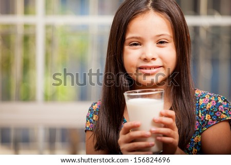 Happy little Latin girl enjoying a glass of milk and smiling